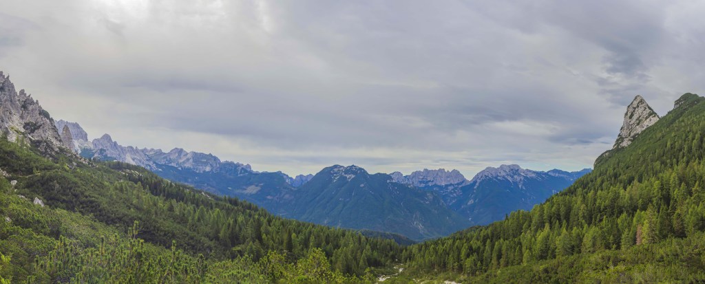 Panorama delle montagne con boschi verdi e nuvole nel cielo.